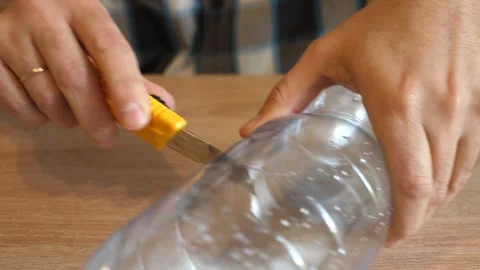 Person cutting an empty plastic bottle with a utility knife on a wooden table 库存影片 341194919