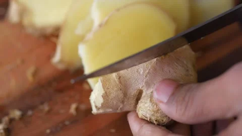 Person cutting fresh ginger root into slices on wooden board with sharp kni.. Stock Footage 332745597