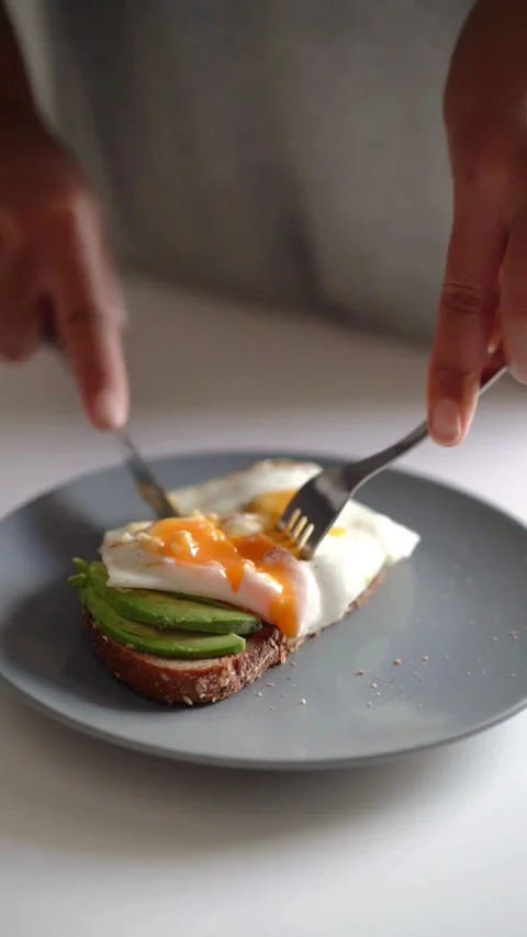 Person cutting a fried egg on avocado toast breakfast Video stock 331772202
