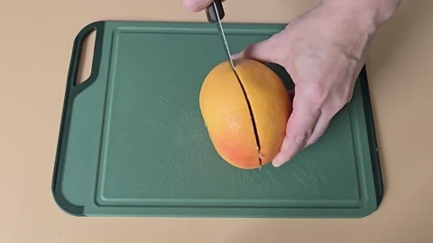 A person cutting a grapefruit in half with a knife on a green cutting board Stock Footage 342027839