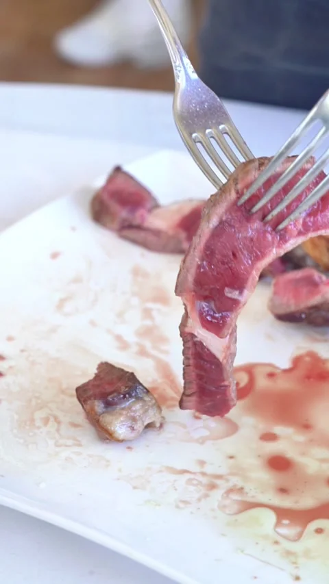 A person is cutting meat with a fork and knife. The meat is on a plate and Stock Footage 327529385