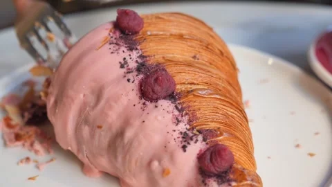 Person cutting pink raspberry croissant on white plate with silver knife an.. Stock Footage 332117622