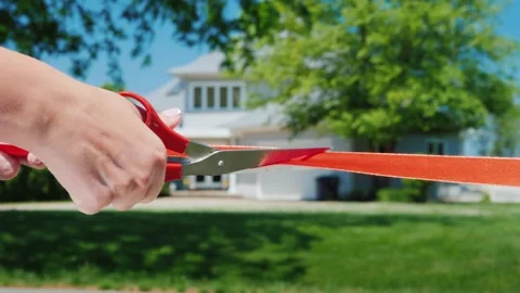 Person cutting red ribbon with scissors in front of new residential house d.. Stock Footage 334551359