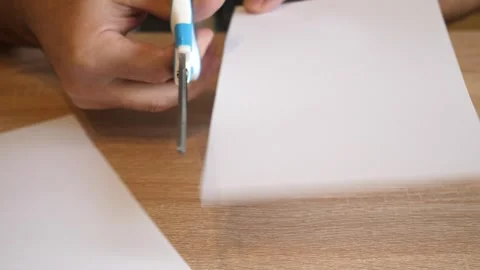 Person cutting a white sheet of paper with scissors on a wooden table in clos Vídeos de archivo 341189738