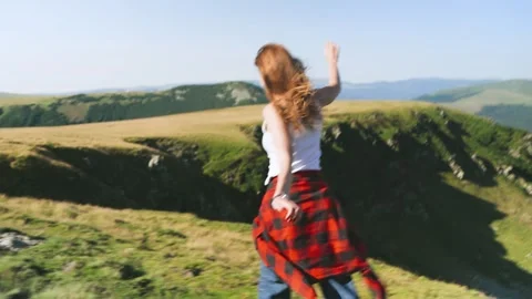 Person dances on grassy hill with a view of mountains on a sunny day in the coun Stock Footage 343840463