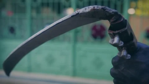 Person in dark gloves holding sharp curved scythe weapon in outdoor setting. Stock Footage 337608047