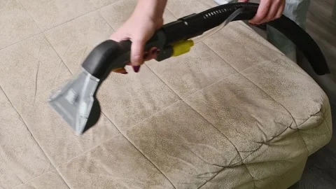Person deep cleans beige sofa upholstery using extractor nozzle to remove dirt Vidéo 347076009