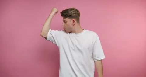 Person demonstrates arm strength in different poses against a pink wall Stock Footage 331990940