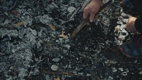 Person digging with a knife in burnt ashes after fire 스톡 동영상 332963141