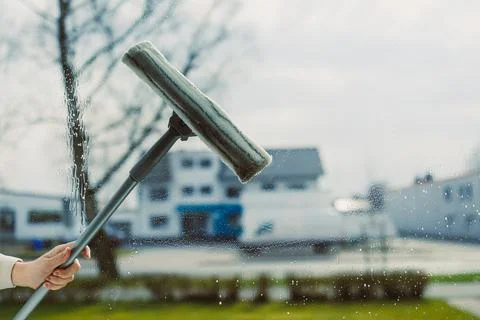 A person is diligently cleaning a window using a squeegee tool on a bright .. Stock Photos
