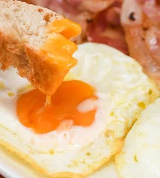 Person Dipping Bread into Fried Egg Yolk for Breakfast 库存照片
