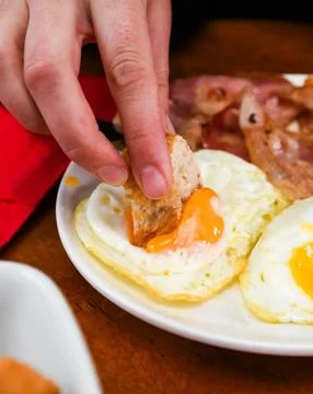 Person Dipping Bread into Fried Egg Yolk for Breakfast Stock Photos