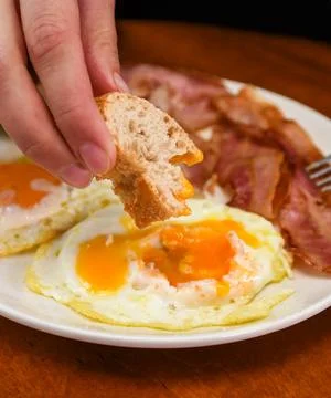 Person Dipping Bread into Fried Egg Yolk for Breakfast 库存照片
