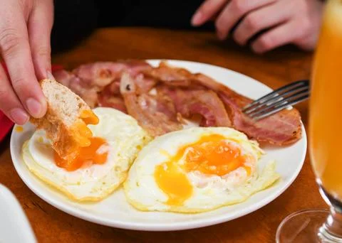 Person Dipping Bread into Fried Egg Yolk for Breakfast Stock Photos