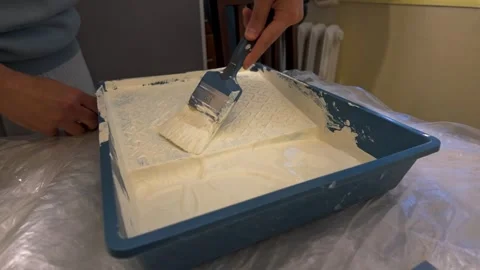 Person dipping paint brush into plastic tray indoors Stock Footage 335314769
