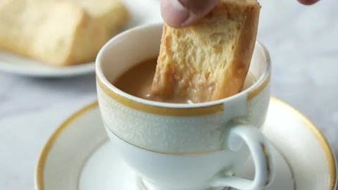 Person dips biscuit into cup of tea, biscuit absorbs liquid, tea time snack. Stock Footage 332578709