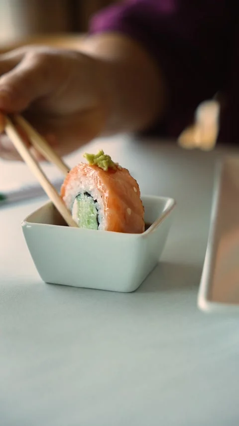 Person dips a salmon sushi roll topped with wasabi into soy sauce using Stock Footage 346718453