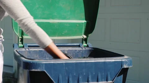 Person disposing black plastic trash bag into blue recycling bin with green.. Stock Footage 334543388