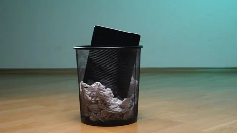 Person disposing of an obsolete tablet computer into a black mesh trash can Video stock 342769283