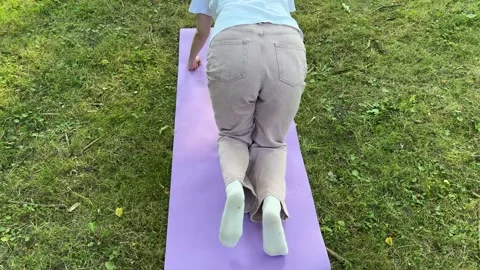 Person doing leg exercises on purple yoga mat outdoors on grass Stockbeeldmateriaal 340149162