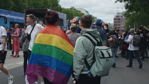 Person draped in a rainbow flag walks among the crowd of Pride parade Stock Footage 346238724