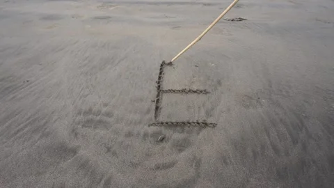 Person drawing letter E on sandy beach 動画素材 198679249