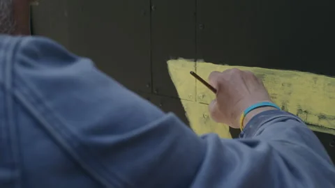 A person draws with yellow paint on a gray surface Stock Footage 261470448