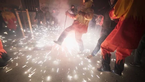 A person dressed as devil jumps over fireworks as it burns on the ground Stock Footage 100375625