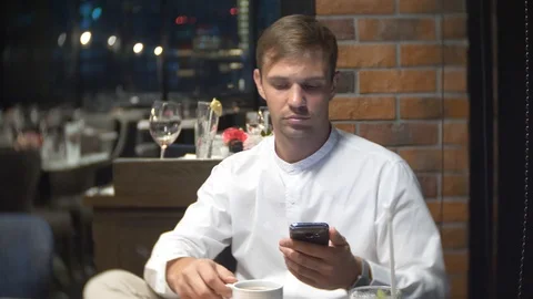 A person drinks coffee, checking a cell phone at night in a restaurant. 4k Video stock 86439899