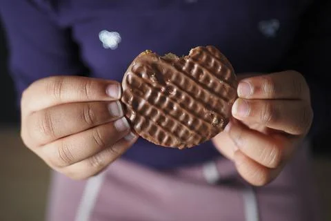 Person eats a chocolate cookie with a bite taken out Stock Photos