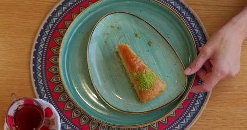 Person eats slice of traditional baklava with pistachios on colorful plate Stock Footage 307606826