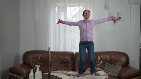 A person energetically dancing on a couch while wearing colorful cleaning gloves Stock Footage 309380222