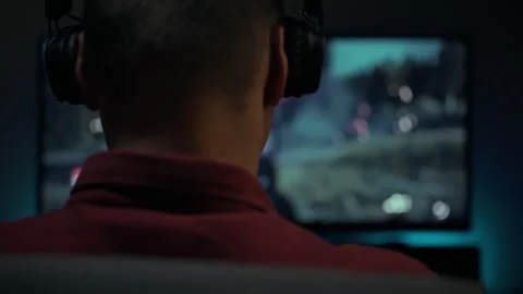 Person engaged in gaming while wearing headphones in a dimly lit room Stock Footage 303649891