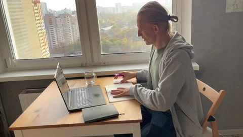 A person engaged in reading and simultaneously working on a laptop by a window Stock Footage 317779065