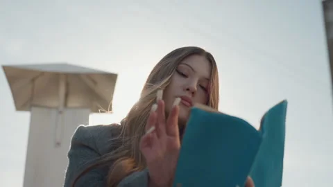 Person enjoying sunlight while studying script beside city buildings. Individual Video stock 345542242