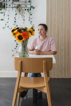 Person enjoys coffee while sitting at a table in a bright room with flowers.. Stock Photos