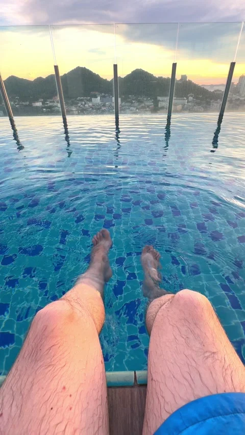 A person enjoys the tranquility of an pool at sunset, with feet dipped in water Video stock 304881780