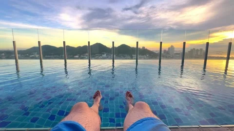 A person enjoys the tranquility of an pool at sunset, with feet dipped in water Stock Footage 305857304