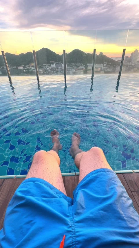 A person enjoys the tranquility of an pool at sunset, with feet dipped in water Stock Footage 305857882