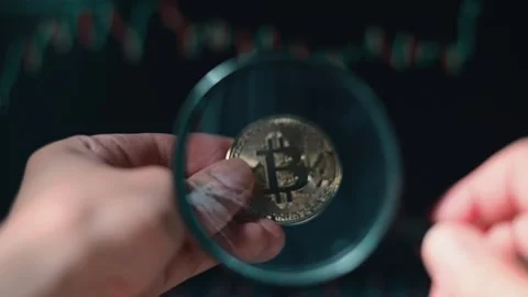 A person examines a bitcoin coin through a magnifying glass, showcasing the Vidéo 338301435