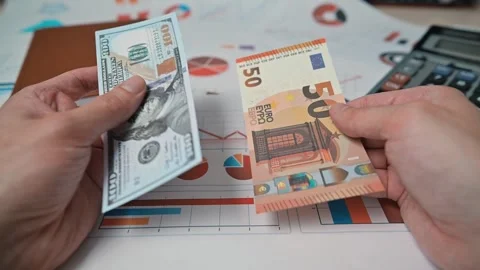 A person examines two different currency notes euro and dollar while seated at a Stock Footage 338301528