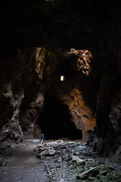 Person exploring a spacious dark cave with a distant light opening and rock.. Stock Photos