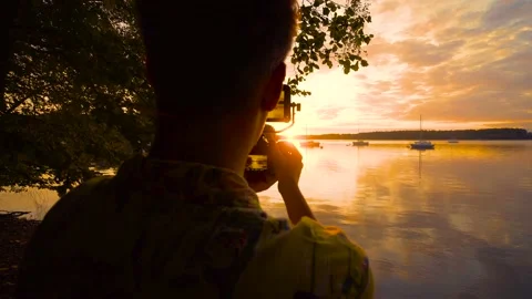 Person filming colorful orange sunset with sony camera at lake with boats 4K Stock Footage