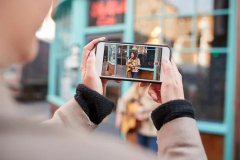Person Filming Female Musician Busking Playing Acoustic Guitar And Singing To Stock Photos