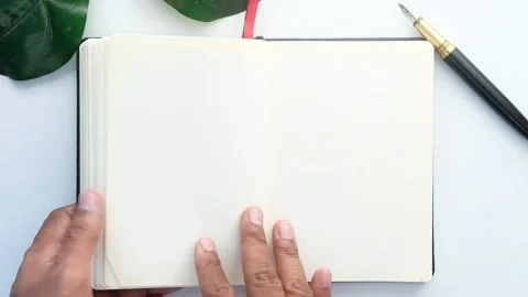 Person flipping pages of blank notebook with pen and plant nearby. Stock Footage 332578432