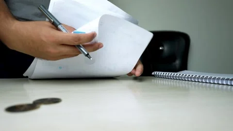 Person flipping through documents on a desk with coins nearby Stock Footage 315982750