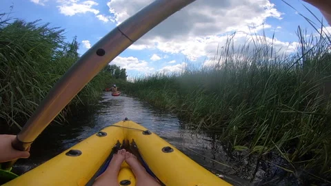 Person floating inflatable boat behind people on SUP board along a narrow river Stock Footage 307757510