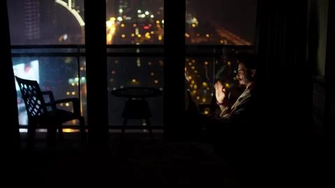 Person focused on remote tasks while enjoying evening ambiance and city skyline Stock-Fotos