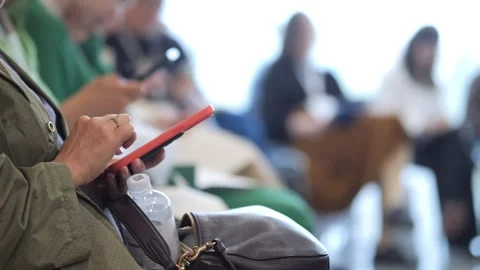 Person focuses on red tablet during event, surrounded by seated attendees Stock Footage 343592193