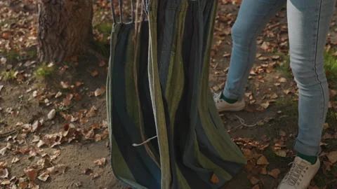 Person folding striped hammock on forest floor during fall day. Woman in green Stock Footage 338007684